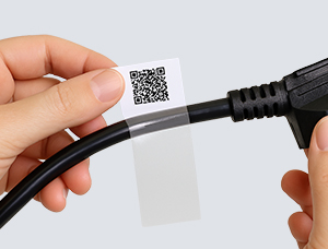 Hände bringen ein Hybrid-Etikett auf ein schwarzes Kabel an. Das Etikett besteht aus einem weißen Abschnitt mit einem gedruckten QR-Code und einem transparenten Laminatbereich.