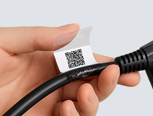Hände halten ein schwarzes Kabel und bringen ein Hybrid-Etikett an. Das Etikett besteht aus einem weißen Abschnitt mit einem gedruckten QR-Code und einem transparenten Laminatbereich, der über das weiße Schriftfeld geklebt wird.