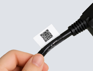 Eine Hand hält ein schwarzes Kabel mit einem weißen Etikett, das einen gedruckten QR-Code zeigt. Das Etikett ist als Fahne um das Kabel gewickelt und der transparente Laminatbereich schützt die Beschriftung dauerhaft.