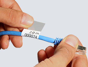 Zwei Hände bringen einen selbstlaminierenden Kabelmarkierer auf ein blaues Ethernet-Kabel auf. Das Etikett besteht aus einem weißen Schriftfeld mit gedruckten Zahlen sowie einem transparenten Laminatbereich, der um das Kabel gewickelt wird.