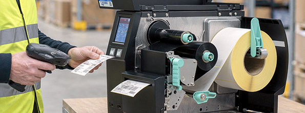 Thermotransferdrucker in der Logistik erstellt Etiketten, die mit einem Handscanner geprüft werden – passend zum Druckverfahren für Logistiketiketten.